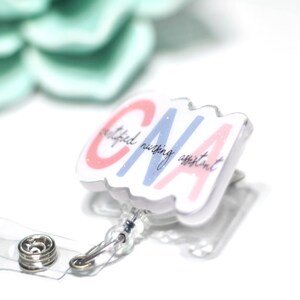 Pode incluir: Um porta-crach&aacute; branco com uma al&ccedil;a de pl&aacute;stico transparente e um fecho de press&atilde;o de metal. O crach&aacute; apresenta as letras "CNA" em rosa e azul, com as palavras "certified nursing assistant" em script. Uma suculenta verde claro no fundo.