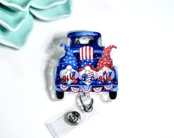 Pode incluir: Um caminhão azul e vermelho com três gnomos na parte de trás. Os gnomos usam chapéus vermelhos e azuis com estrelas brancas. O caminhão tem uma faixa vermelha, branca e azul pendurada na parte de trás. O caminhão está em um carretel de crachá de acrílico transparente.