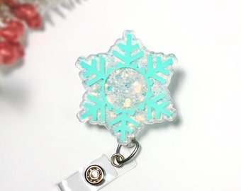May include: A white snowflake-shaped badge holder with a light blue snowflake design and glitter accents. The badge holder has a clear plastic clip.