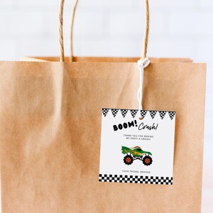 May include: A brown paper gift bag with a white string handle. A black and white tag with a monster truck graphic and the text "BOOM! Crash! Thank you for making my party a SMASH! Your friend, Brooke" is attached to the bag.