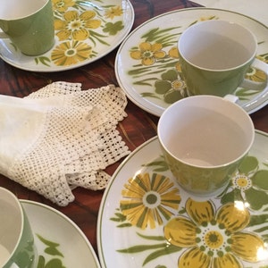 Könnte beinhalten: Ein Set mit vier grünen und gelben floralen Teetassen und Untertassen. Die Tassen und Untertassen haben einen weißen Hintergrund mit einem grünen und gelben floralen Muster.
