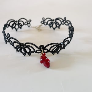 May include: A black lace choker necklace with a dangling red heart charm.