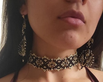 May include: A black beaded choker necklace and matching earrings with a gold pattern. The earrings and choker are black with gold beads. The top is a burgundy colour.