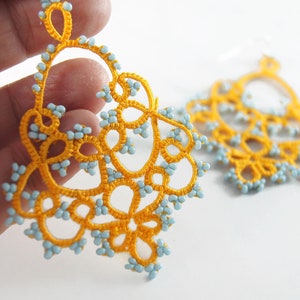 May include: A pair of yellow and blue beaded earrings with a delicate, intricate design. The earrings are made with small beads and have a dangling, floral-like shape.