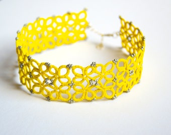 May include: A yellow crocheted choker necklace with silver beads. The necklace is made of delicate, intricate crocheted flowers.