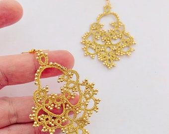 May include: A pair of gold-tone dangle earrings with a delicate, intricate design. The earrings are made of small beads and wire, and they have a slightly teardrop shape.