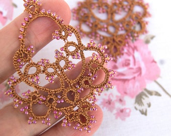May include: A pair of delicate, brown lace earrings with pink beads. The earrings are hand-crafted and feature an intricate design.