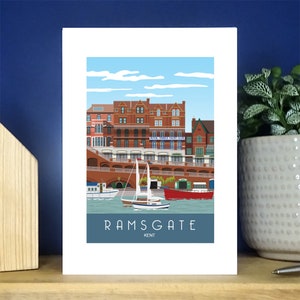 Puede incluir: Una ilustración colorida de Ramsgate, Kent, Inglaterra. La ilustración presenta una fila de edificios de ladrillo con un cielo azul y nubes blancas en el fondo. Hay barcos en el agua frente a los edificios. El texto "RAMSGATE KENT" está en la parte inferior de la ilustración.