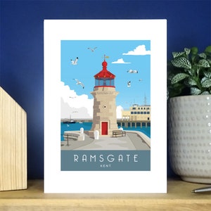 Puede incluir: Una ilustración colorida de un faro en un muelle en Ramsgate, Kent. El faro es rojo y blanco con un cielo azul y gaviotas en el fondo. El texto "RAMSGATE KENT" está debajo del faro.