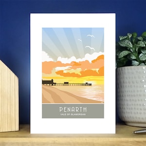 May include: A colorful illustration of a pier in Penarth, Wales. The pier extends out into the ocean with a sunset in the background. The text "Penarth" and "Vale of Glamorgan" is at the bottom of the image.