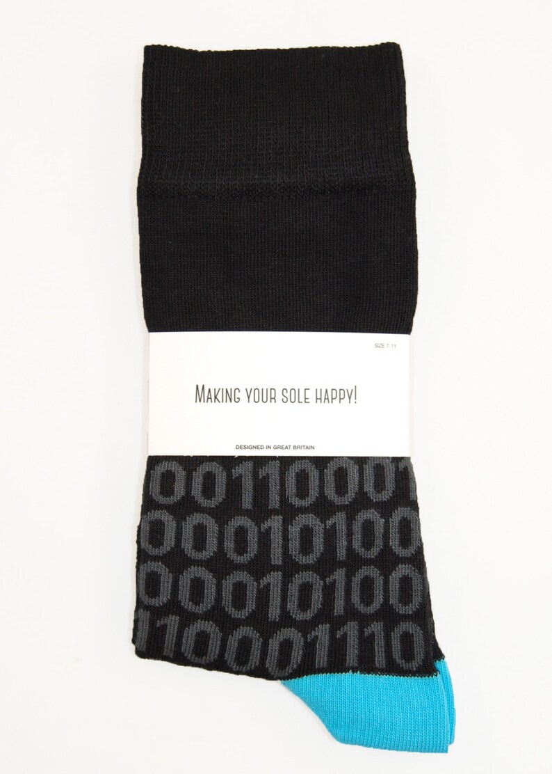 Op de afbeelding: Zwarte sokken met een blauwe rand en een grijs binair codepatroon. De sokken hebben een wit label met de tekst "Making your sole happy!" en "Designed in Great Britain".