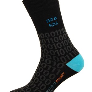 Op de afbeelding: Zwarte sokken met een blauw en oranje ontwerp met de tekst "EASY AS 01,10,11" en "THOSE WHO UNDERSTAND BINARY. THOSE WHO DON'T." De sokken zijn bedekt met een patroon van 0's en 1's.