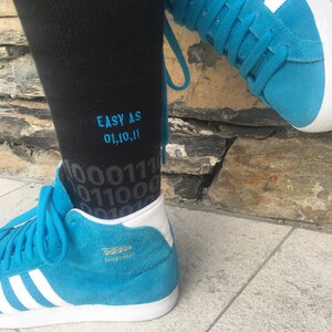 Op de afbeelding: Een paar blauwe high-top sneakers met witte strepen en een zwarte sok met de tekst "EASY AS 01,10,11" erop geborduurd.