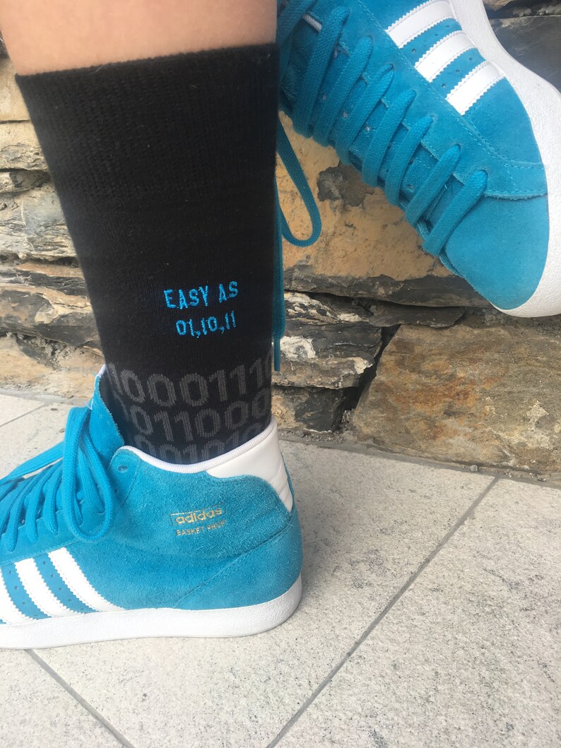 Op de afbeelding: Een paar blauwe high-top sneakers met witte strepen en een zwarte sok met de tekst "EASY AS 01,10,11" erop geborduurd.