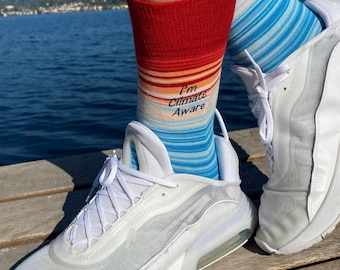 Puede incluir: Zapatillas blancas con una parte superior de malla transparente y un calcetín a rayas azul y naranja que dice "I'm Climate Aware".