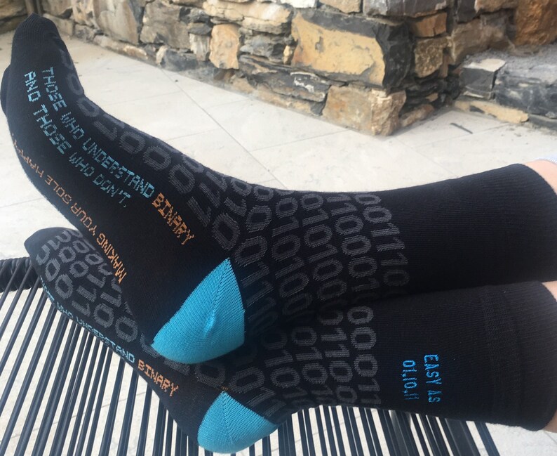Op de afbeelding: Zwarte sokken met een blauw en oranje ontwerp met de tekst "Those who understand binary and those who don't. Making your sole easy as 011011."