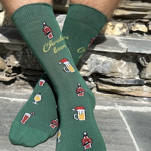May include: Green Christmas beer socks with a red and white beer bottle, beer mug, and candy cane design. The socks have the text "Christmas Beers" on them.