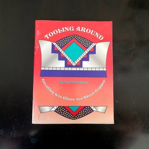 May include: A red book titled "Tooling Around: Creating with Glass and Sheet Copper" by Ray Bain Weiner. The cover features a colourful geometric design with turquoise, red, yellow, and blue.
