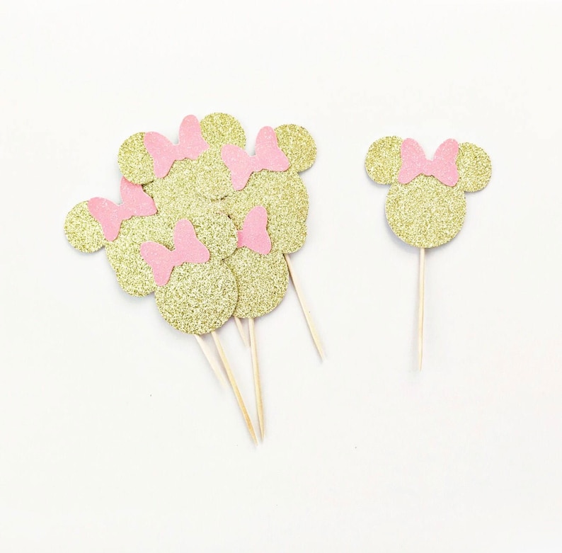 Puede incluir: Un conjunto de 7 adornos para cupcakes de Minnie Mouse con purpurina dorada y lazos rosas. Los adornos est&aacute;n en palitos de madera.