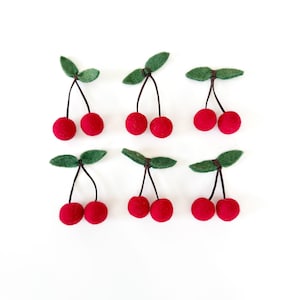 May include: Six pairs of felt cherries with green felt leaves. The cherries are red and the stems are brown.