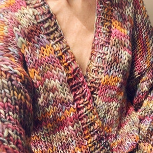 Pode incluir: Um casaco de malha grossa e colorido com um decote em V profundo. O casaco é feito com uma variedade de tons de rosa, laranja, marrom e roxo.