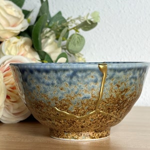 May include: A blue and brown ceramic bowl with gold accents. The bowl has a crackled glaze and a unique design.