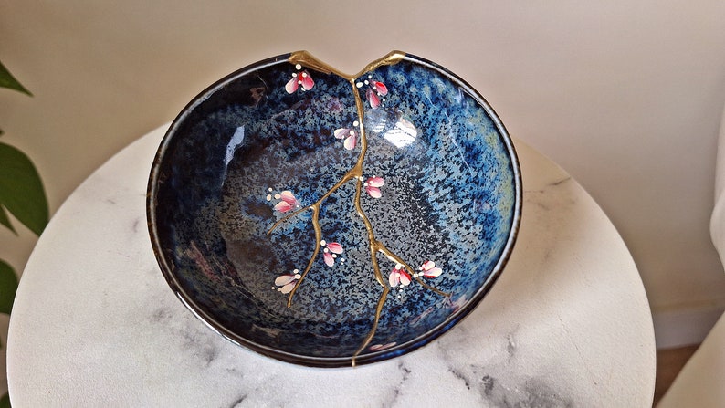 Peut inclure: Un bol en c&eacute;ramique bleu avec une fissure r&eacute;par&eacute;e &agrave; la peinture dor&eacute;e. Le bol est d&eacute;cor&eacute; d'une branche dor&eacute;e et de fleurs roses.
