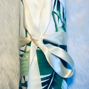 May include: A white and green fabric roll with a tropical leaf print is tied with a cream-coloured satin ribbon.