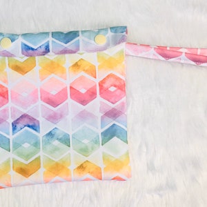 May include: A colourful reusable wet bag with a geometric pattern and a snap closure. The bag has a pink handle and is made of waterproof fabric.