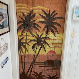 May include: A brown bamboo beaded curtain with a sunset and palm tree design. The curtain is hanging in a doorway.