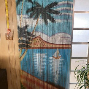 May include: A blue and brown bamboo beaded curtain with a painted scene of palm trees, a beach, and a sailboat. The curtain is hanging in a doorway.