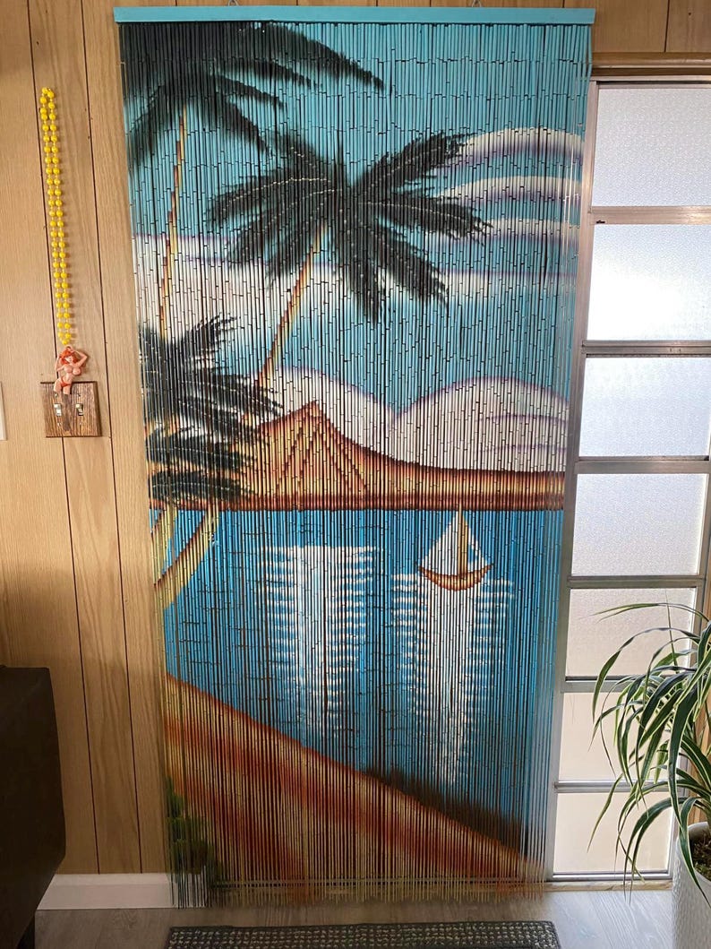 May include: A blue and brown bamboo beaded curtain with a painted scene of palm trees, a beach, and a sailboat. The curtain is hanging in a doorway.