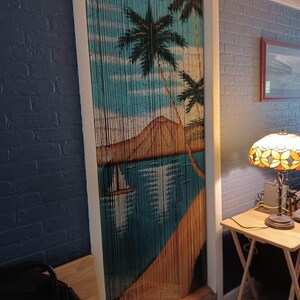 May include: A blue and brown beaded door curtain with a tropical island scene. The curtain features palm trees, a beach, and a mountain.
