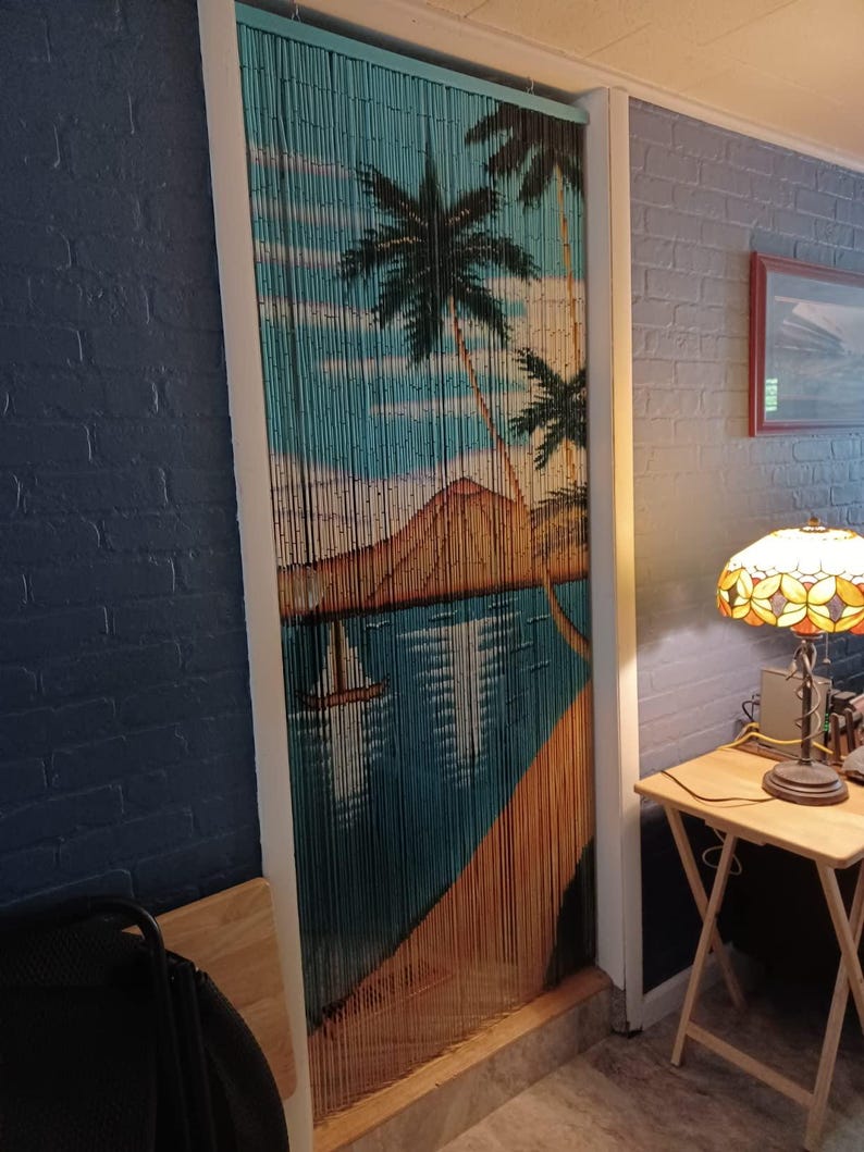 May include: A blue and brown beaded door curtain with a tropical island scene. The curtain features palm trees, a beach, and a mountain.