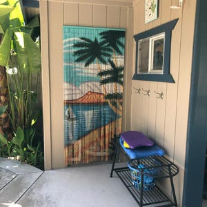 May include: A black metal shelf with a blue basket and a purple and blue surfboard on top. The shelf is in front of a wall with a tropical-themed beaded curtain and a window with a blue frame.
