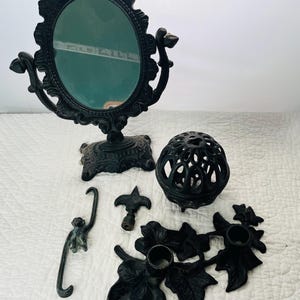 May include: A set of black cast iron decorative items, including a vanity mirror, a round cage, a candle holder, a hook, and a finial.
