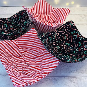 May include: Four fabric bowl cozies in a Christmas theme. Two are red and white striped, and two are black with green holly and red candy canes.