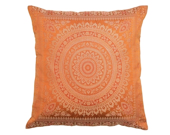 May include: Square orange cushion featuring a gold circular pattern. The cushion has a floral design around the edges and a detailed pattern in the centre. The cushion is made of a soft, textured fabric.
