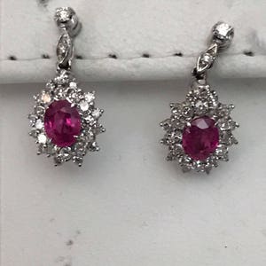 Könnte beinhalten: Ein Paar silberne Ohrringe mit einem Rubin-Edelstein, der von Diamanten umgeben ist.