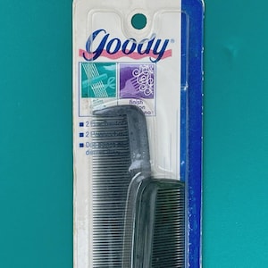 May include: A black comb with a handle, packaged in a clear plastic and cardboard backing. The packaging features the brand name "Goody" in pink and white, along with product information and illustrations.