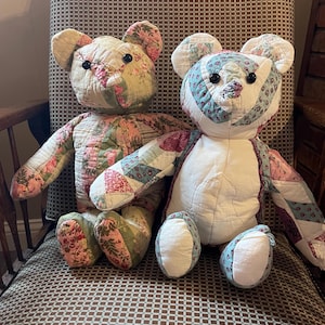 May include: Two patchwork teddy bears sit on a patterned chair. The bears are made from fabric with floral and geometric patterns, featuring button eyes and stitched details. One bear has a cream body, the other a white body.