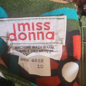 May include: Close-up of a vintage dress label with the text "miss donna" in red. The label also includes washing instructions and a size 10 tag. The dress features a colorful floral pattern with green, blue, red, and white elements.