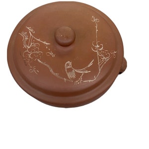 May include: A terracotta teapot with a lid and a bird design. The teapot has a brown glaze and a white bird design on the side.