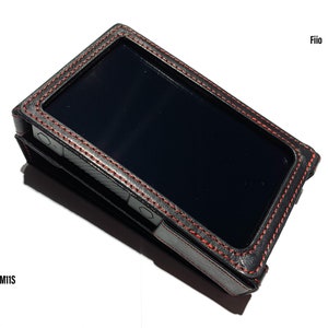 May include: Black leather case with red stitching for a digital audio player. The case has a rectangular shape with a screen visible in the center. The brand name "Fiio" is printed on the top right corner, and "M11S" is printed on the bottom left corner.