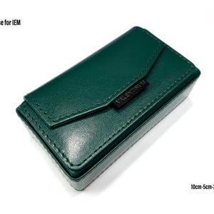 May include: A dark green leather case for in-ear headphones. The case has a flap that closes with a magnetic snap. The case measures 10 cm by 5 cm by 3 cm.