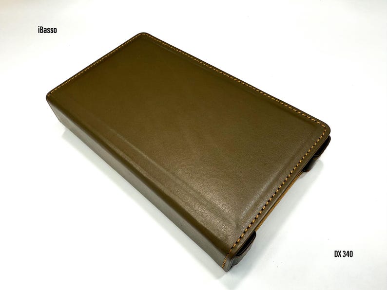 Puede incluir: Funda de cuero verde oliva con bordes cosidos. La funda tiene forma rectangular y est&aacute; etiquetada como "iBasso" y "DX 340". Parece estar dise&ntilde;ada para guardar un peque&ntilde;o dispositivo electr&oacute;nico.