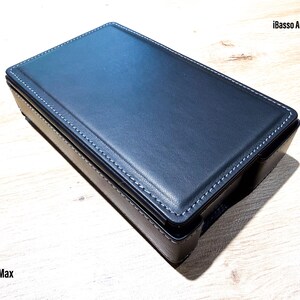 Pode incluir: Uma capa retangular de couro azul-escuro para o leitor de áudio digital iBasso Audio DX340 Max. A capa apresenta costuras brancas visíveis ao longo das bordas e uma superfície lisa de cor sólida, projetada para acomodar o dispositivo.