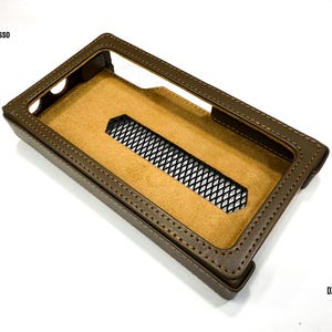Puede incluir: Funda de cuero marr&oacute;n para reproductor de audio digital. La funda tiene forma rectangular con un borde cosido y un interior beige. Tiene una abertura cubierta con malla y los textos "iBasso" y "DX 340" son visibles.