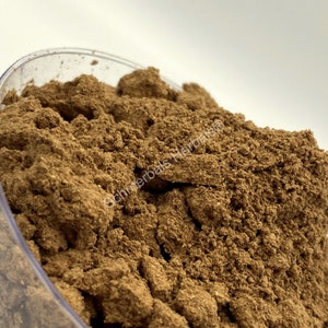 May include: Close-up of a brown powder in a clear container. The powder is finely ground and has a slightly rough texture.