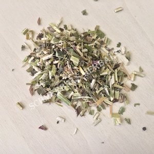 May include: A close-up of a pile of dried herbs, including green, brown, and purple pieces. The herbs are scattered on a light wood surface.